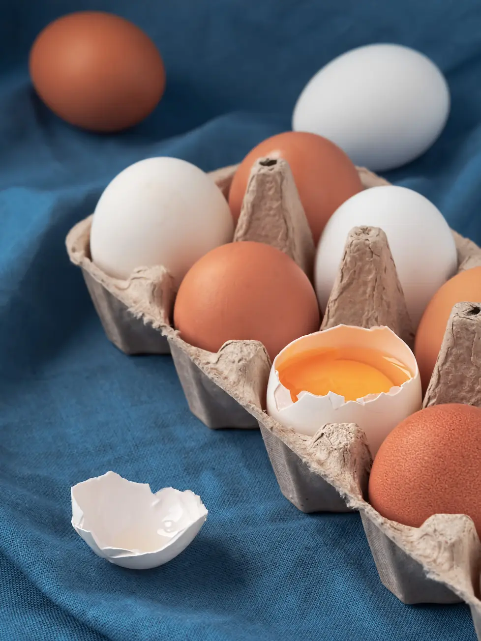 Brown and white farm eggs in a carton with one cracked yolk visible