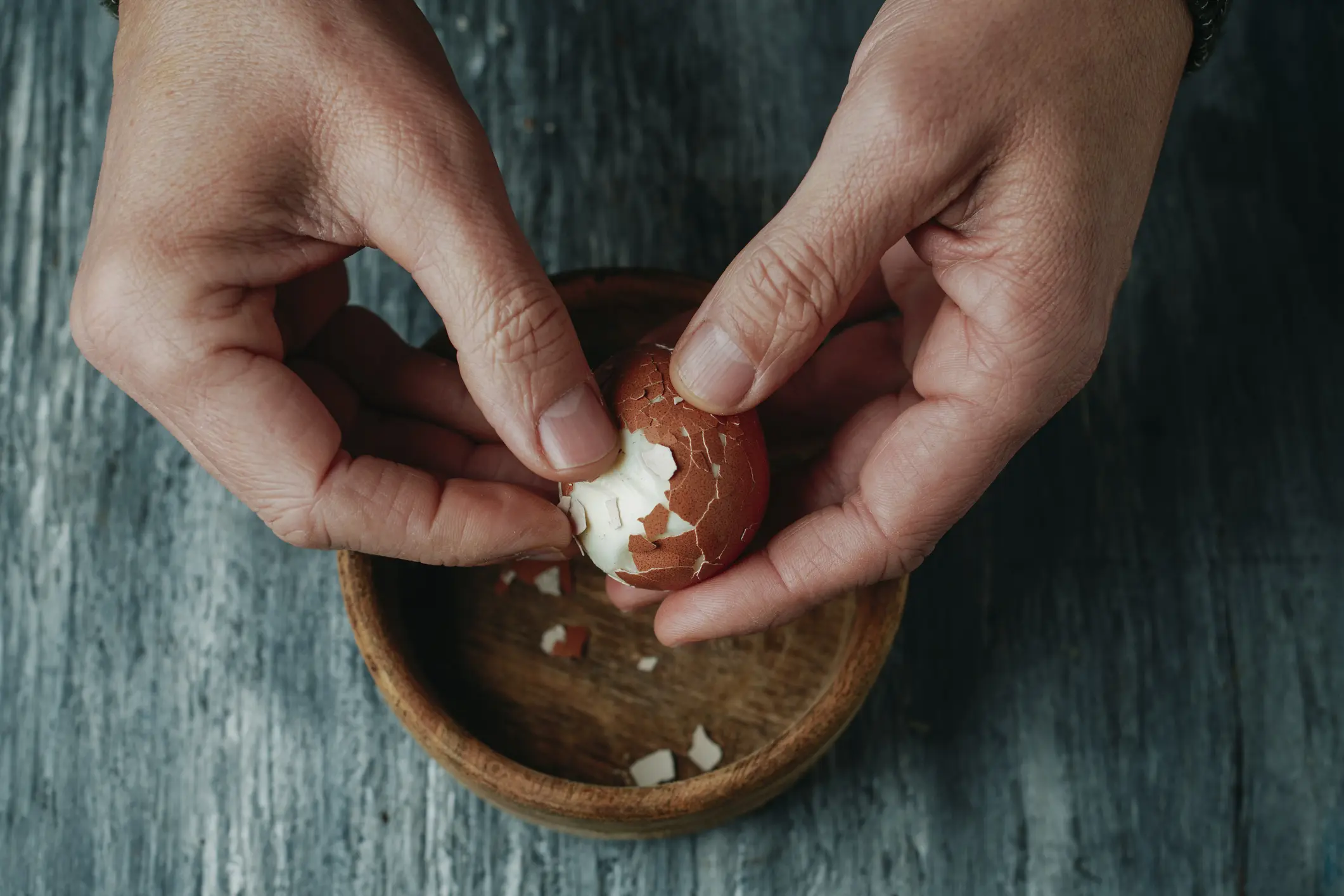Hands peeling a freshly hard‑boiled brown egg from Negri Eggs coop